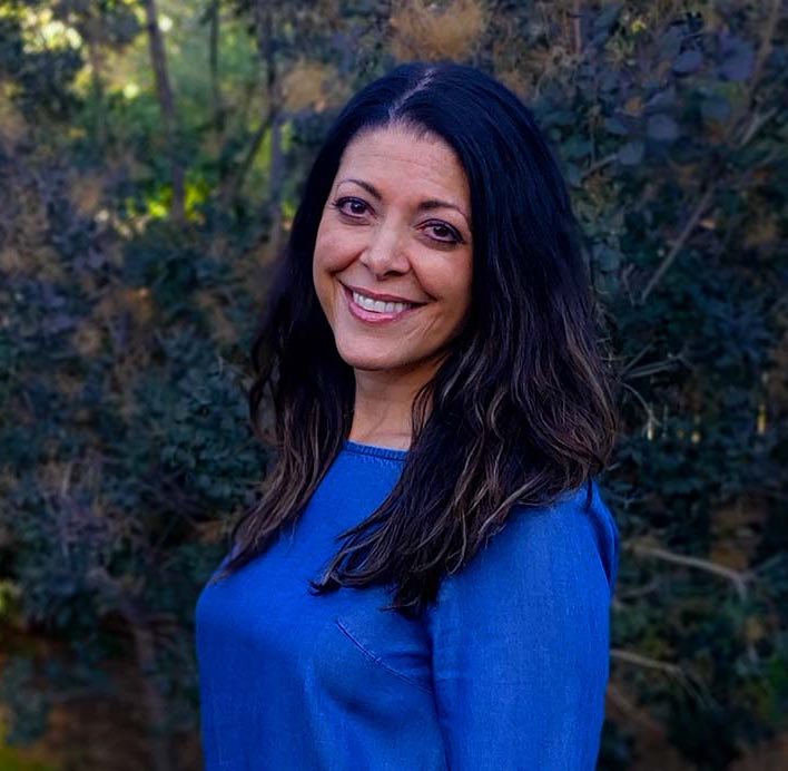A portrait photo of Stacy Dicker outside with greenery behind her.