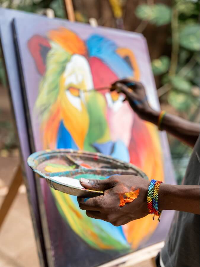Vertical close-up of the hands of an african painter using brush to paint a colorful lion in a patio
