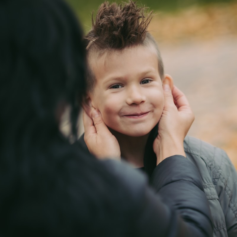 A mother holding the face of a smiling kid between her hands.
