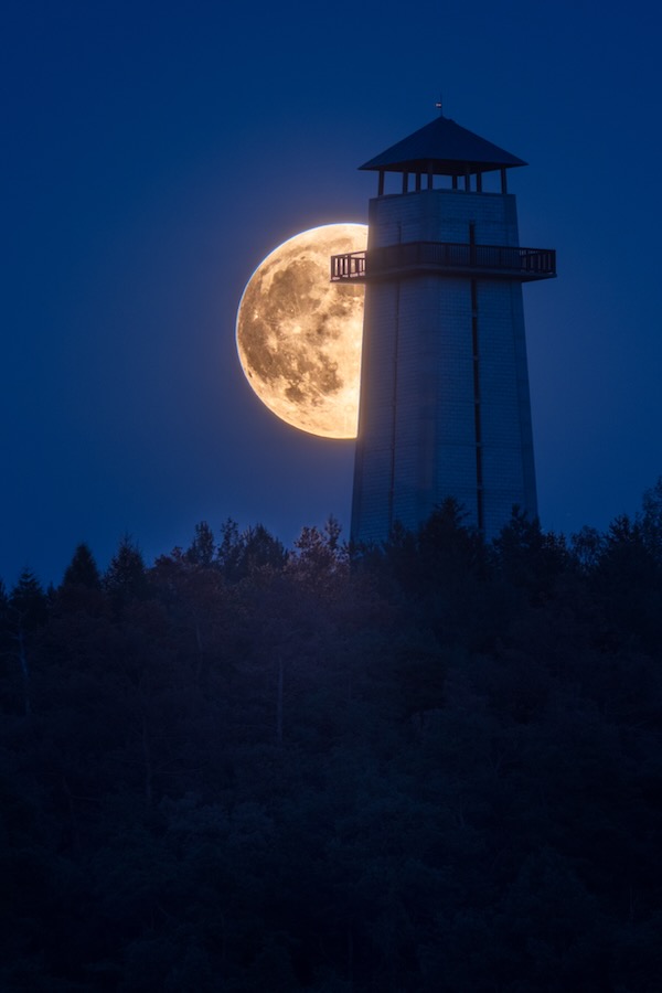 A full moon rising behind a lighthouse.