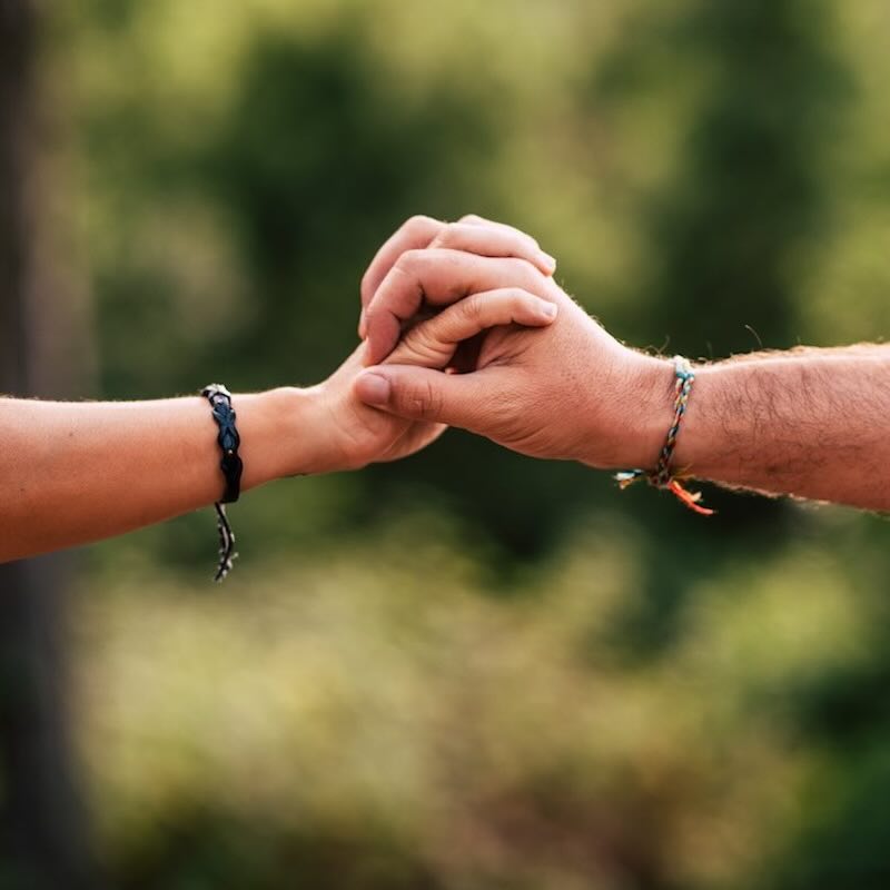 Two hands holding each other with the blurred woods behind them.