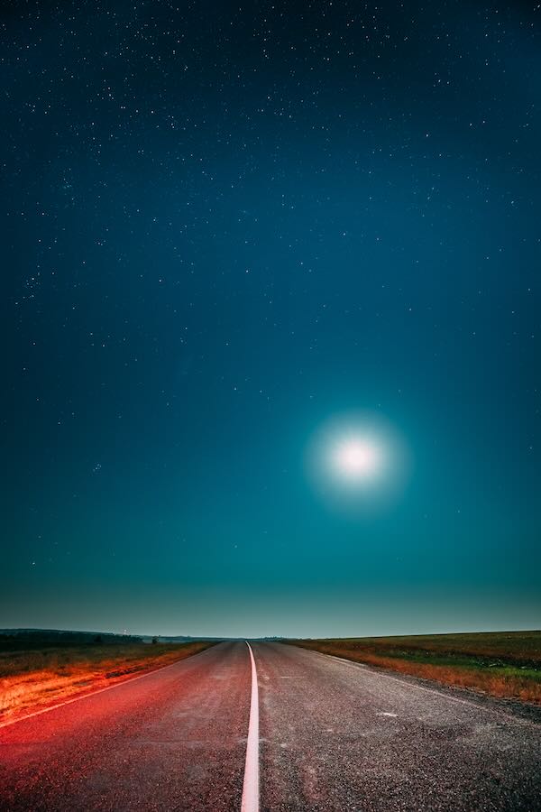 The moon at night shining down on a dark highway.
